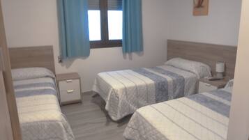 Un dormitorio con dos camas individuales, una mesita de noche con lámpara y una ventana con cortinas.