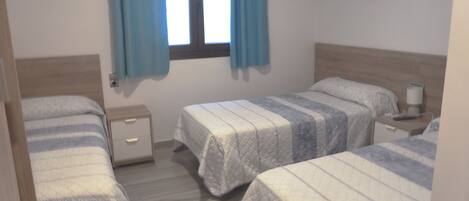 A bedroom with two single beds, a nightstand with a lamp, and a window with curtains.