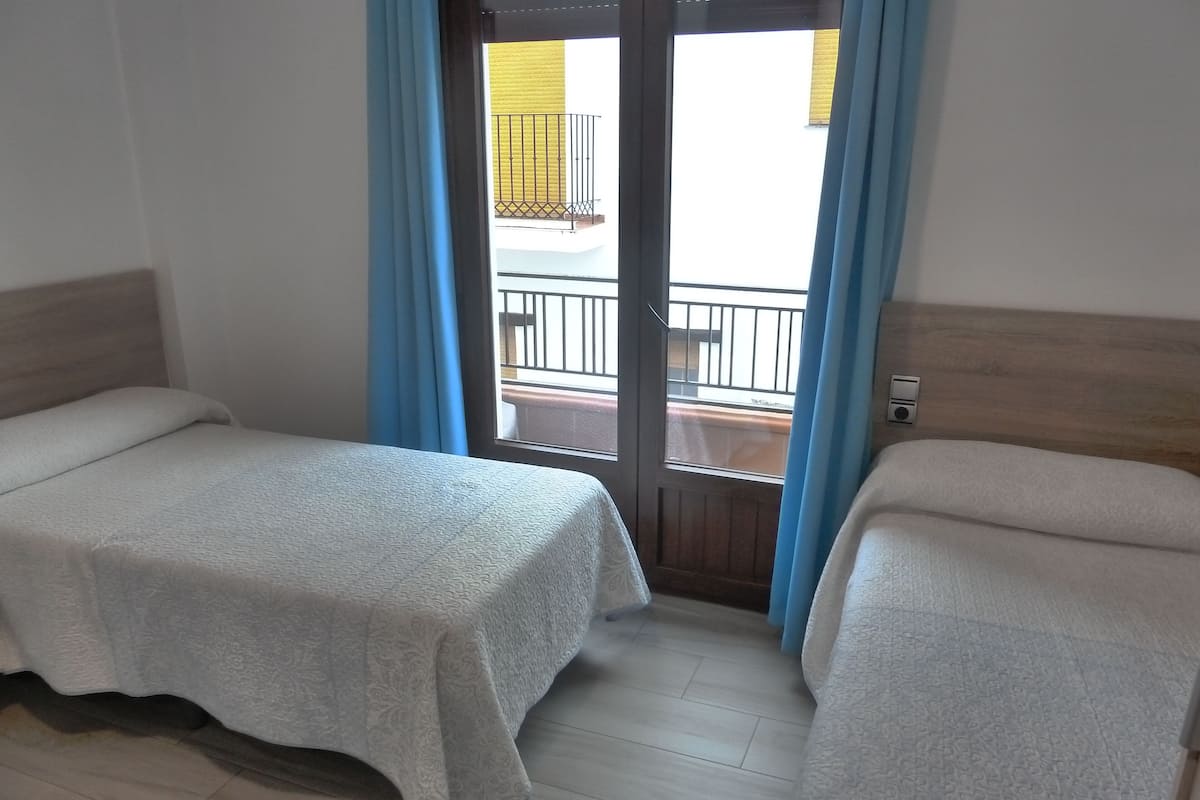 Ein Hotelzimmer mit zwei Einzelbetten, einem Holzkopfende, einem Holzboden und Blick auf einen Balkon mit Geländer.