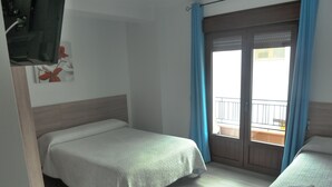 A hotel room with two single beds, a wooden floor, a balcony with blue curtains, and a view of the outside.