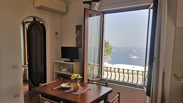 A dining area with a table, chairs, and a view of the sea through a balcony. - Sea View in Positano 1 (Positano)