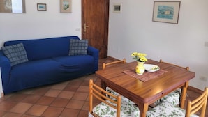 A room with a blue sofa, a wooden dining table with chairs, a wooden door, and wall-mounted lights. - Sea View in Positano 1 (Positano)