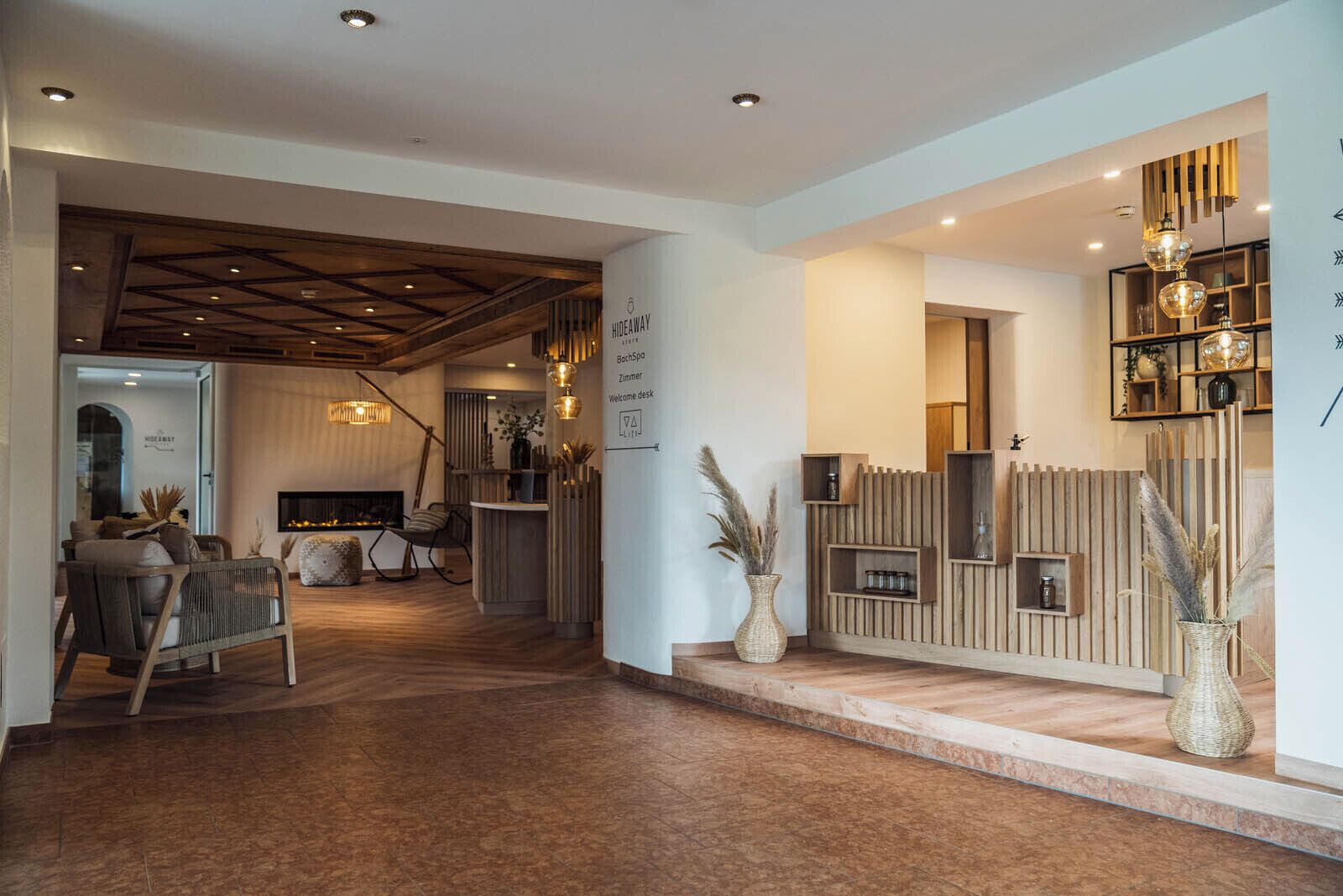 A modern interior with a wooden reception desk, a fireplace, and a seating area with a sofa and chairs.