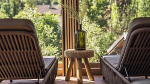 A balcony with two wicker chairs, a small stool with a vase of dried flowers, and a view of a green landscape. - Bergrose Hideaway (Strobl)