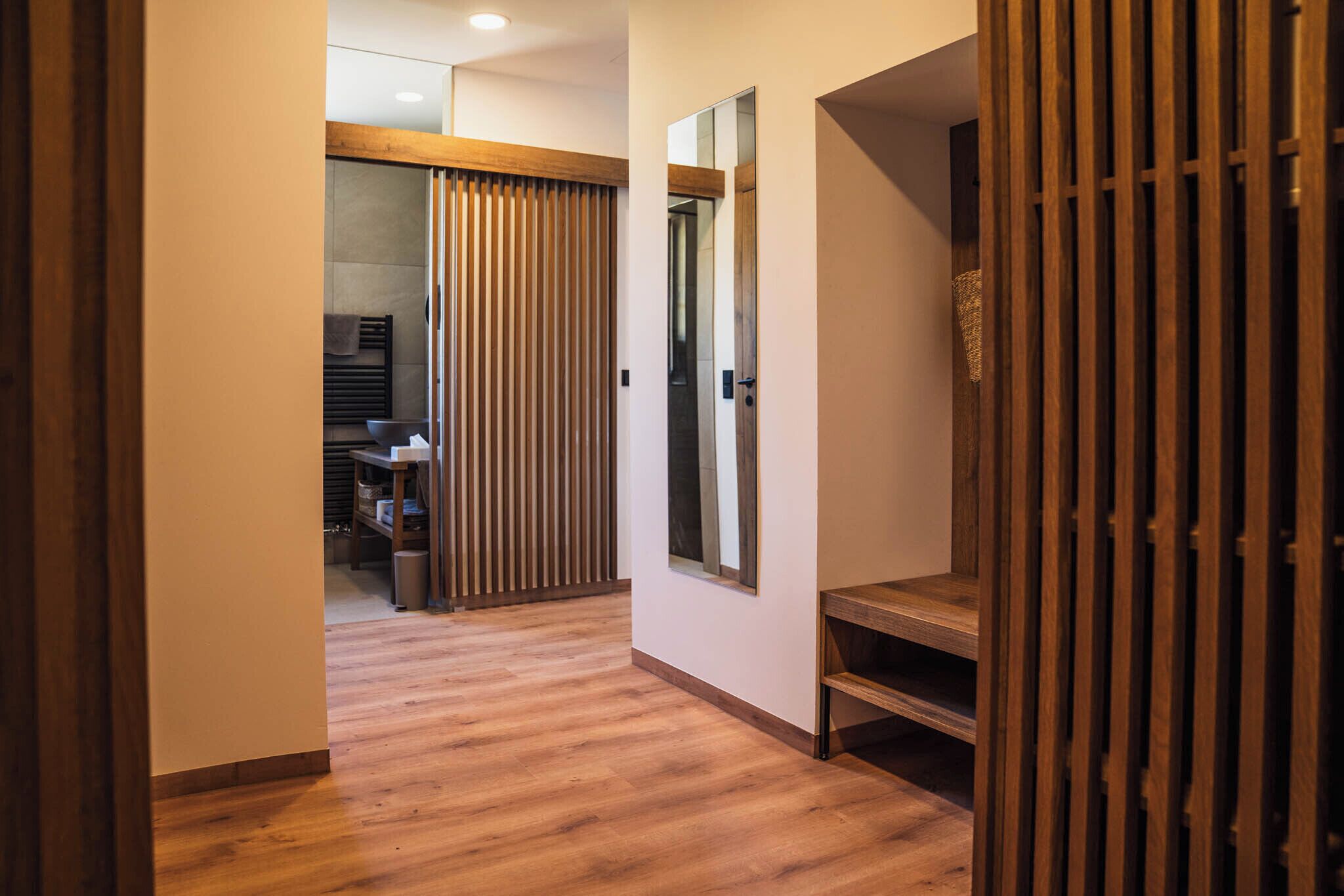 A hallway with wooden flooring, a sliding door, and a mirror on the wall.