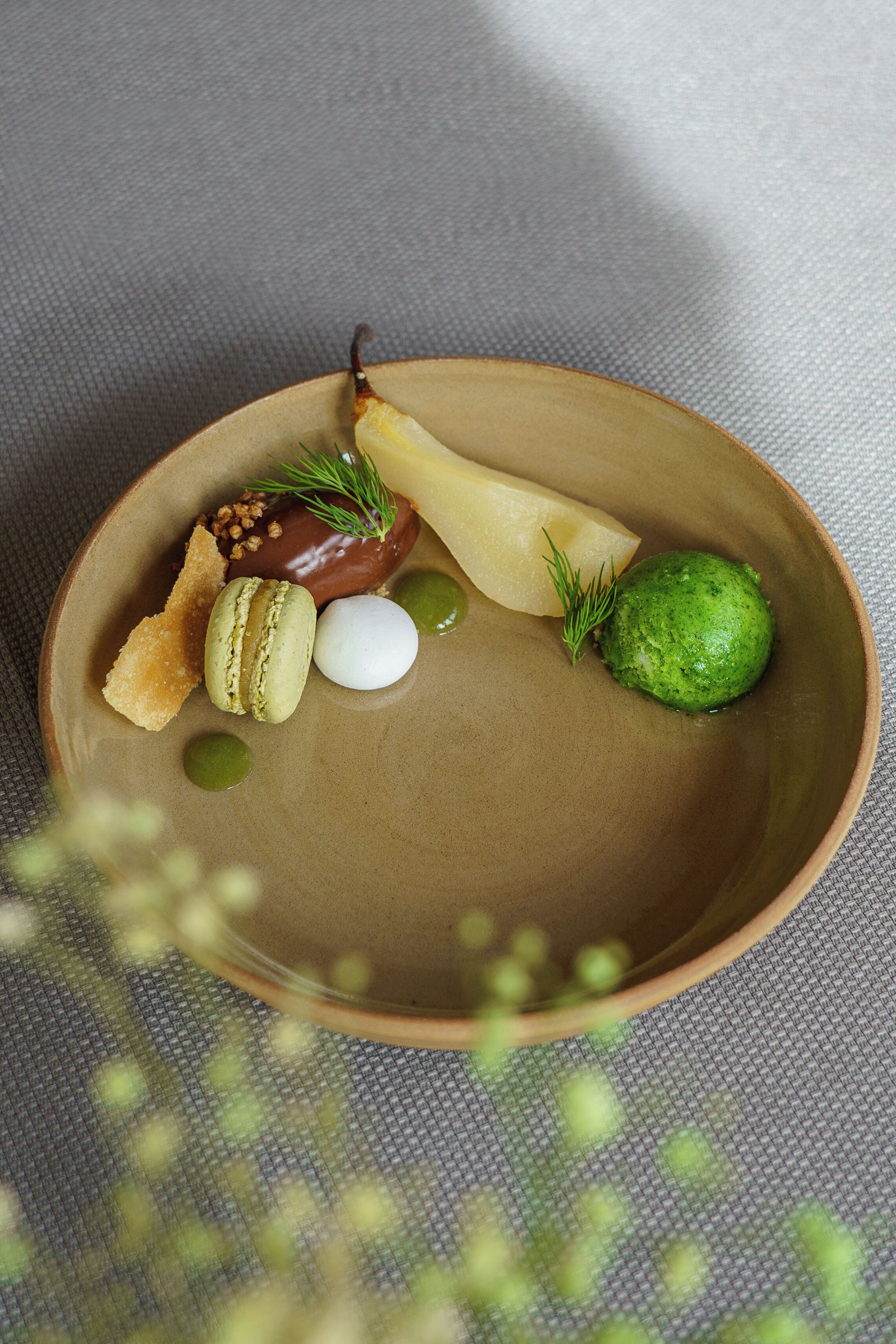 Un plato de cerámica con diversos alimentos, incluyendo una esfera verde, una esfera blanca, una hoja verde y un objeto marrón.