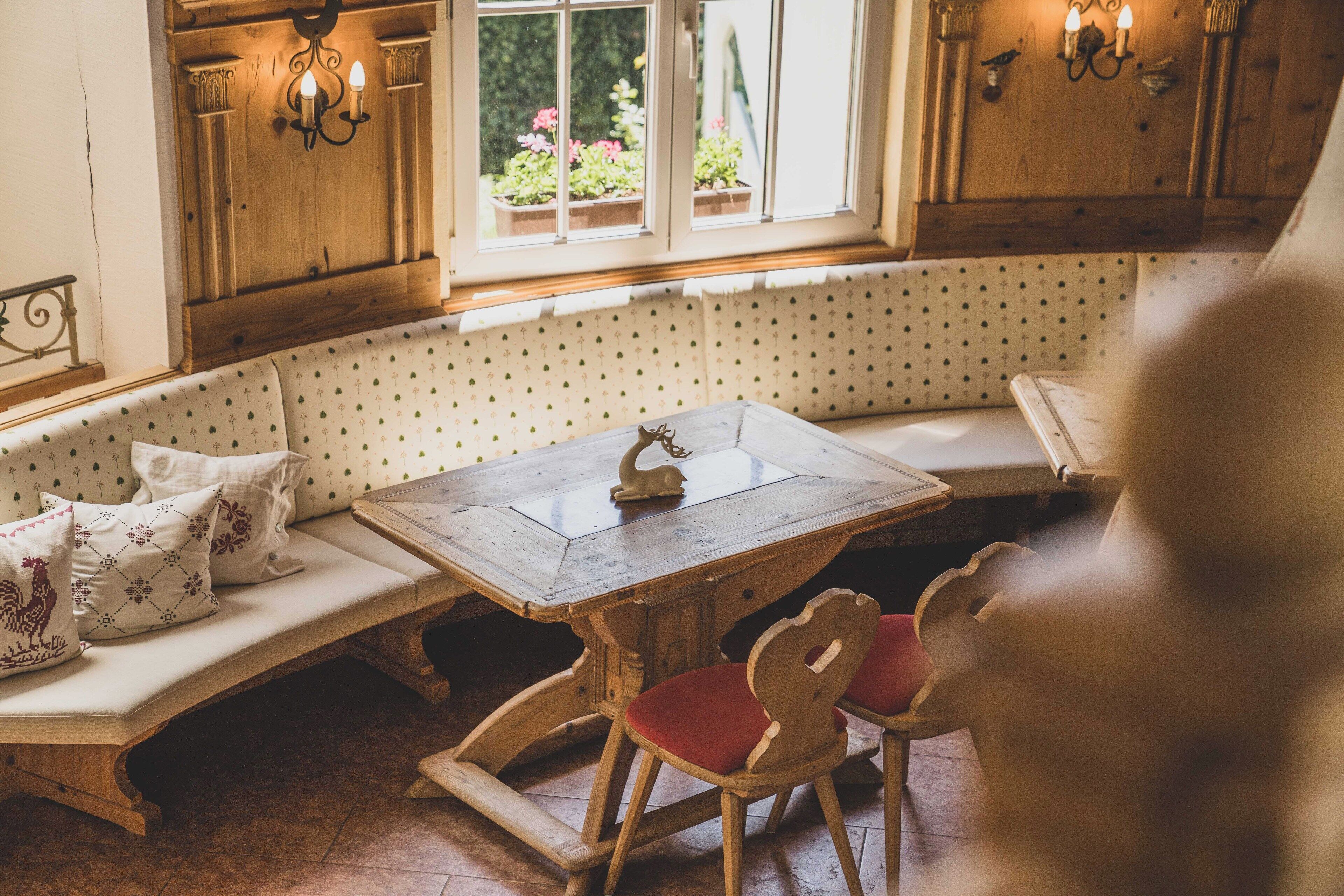 A cozy kitchen with a wooden bench, a dining table, and a window with potted plants.