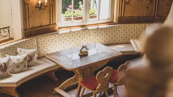A cozy kitchen with a wooden bench, a dining table, and a window with potted plants.