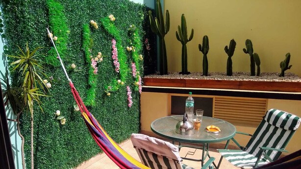 A hammock chair set up on a patio with a green wall and cacti in the background. - Cómodo, Amplio y Seguro Apartamento Familiar a Pasos del Metro en Buenos Aires (Buenos Aires)