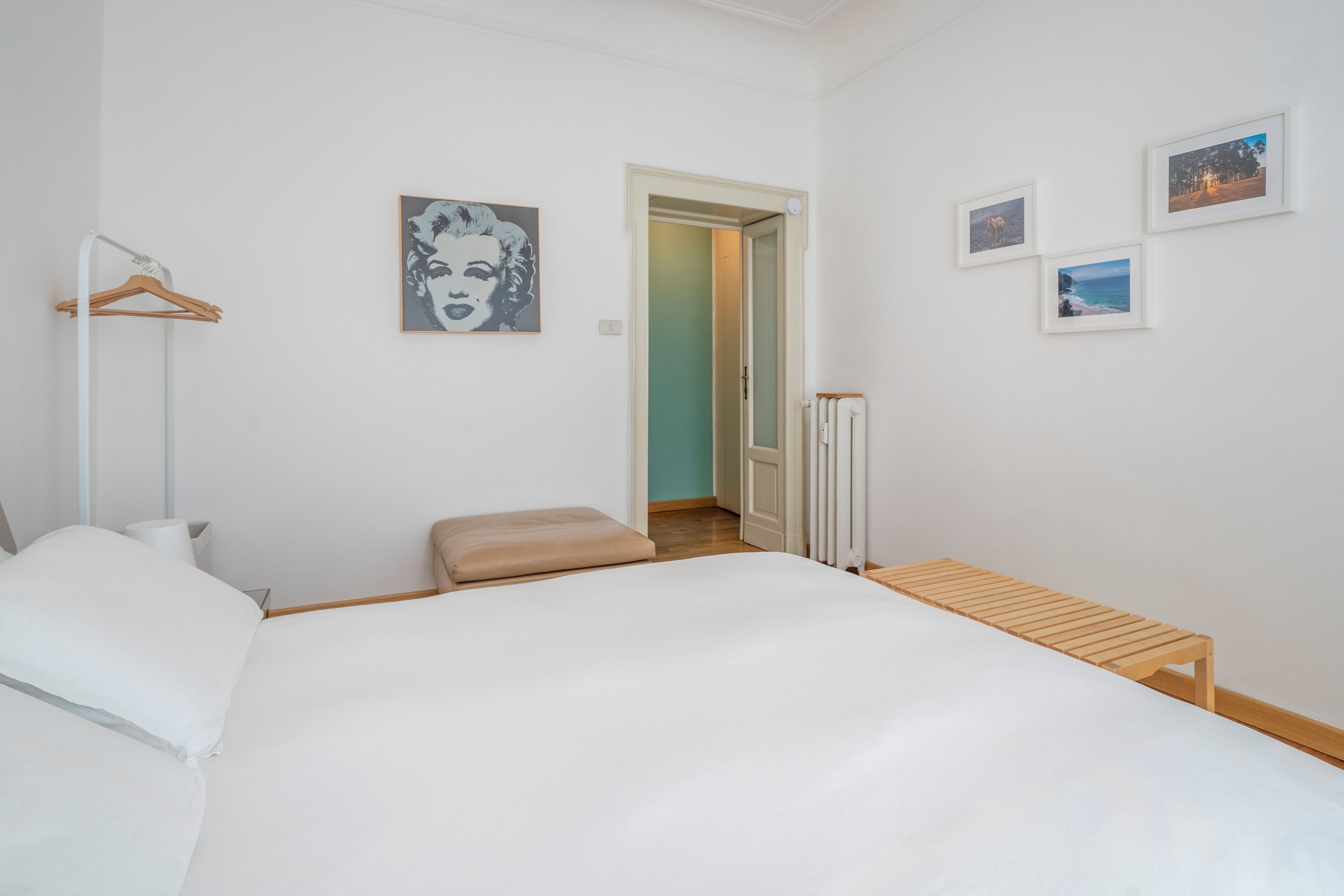 Une chambre à coucher avec un lit, un banc en bois, un radiateur et trois tableaux encadrés accrochés au mur.