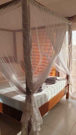 A bed with a white canopy, a wooden headboard, and a patterned cushion. - Amour Sénégal (Ngaparou)