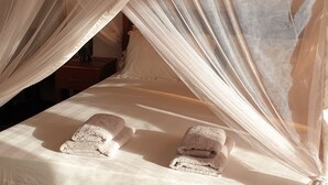 A bed with a wooden frame and white bedding, covered by a white canopy. - Amour Sénégal (Ngaparou)