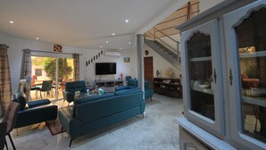A spacious living room with a large blue sofa, a flat-screen TV, and a staircase leading to an upper level. - Amour Sénégal (Ngaparou)