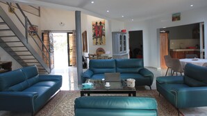 A spacious living room with blue sofas, a glass coffee table, and a staircase leading to another level. - Amour Sénégal (Ngaparou)