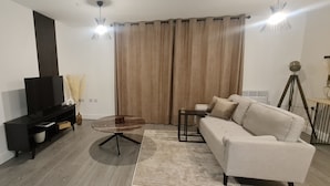 Un salon moderne avec un téléviseur à écran plat, un canapé, une table basse et une lampe.