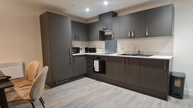 Une cuisine moderne avec des meubles de couleur sombre, un plan de travail blanc et un four encastré.