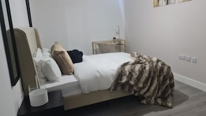 Une chambre à coucher moderne avec un lit, une table de chevet, une lampe et un miroir.