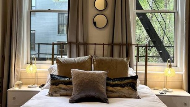 Une chambre à coucher avec un lit, deux tables de chevet, une fenêtre avec des rideaux et une vue sur un arbre à l’extérieur.