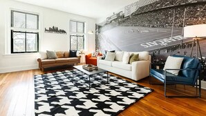 Un salon avec deux canapés, un tapis à motifs et une grande fresque murale sur le thème du sport.