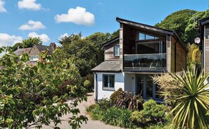 A two-story house with a balcony, surrounded by greenery and a clear sky. - Stylish Estuary View | Sleeps 6 | Parking & Balconies (Saint Ives)