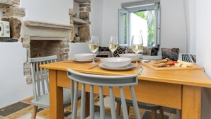 A dining table with white plates, two glasses of white wine, and a wooden cutting board with cheese and crackers. - Serenity Village (Naxos)