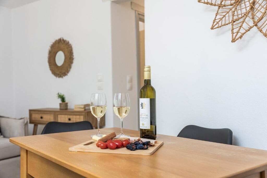 A dining table with a bottle of wine, two glasses, and a wooden board with fruits and bread.