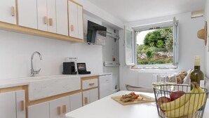 A modern kitchen with white cabinets, a built-in microwave, a sink, and a window with a view of greenery. - Serenity Village (Naxos)