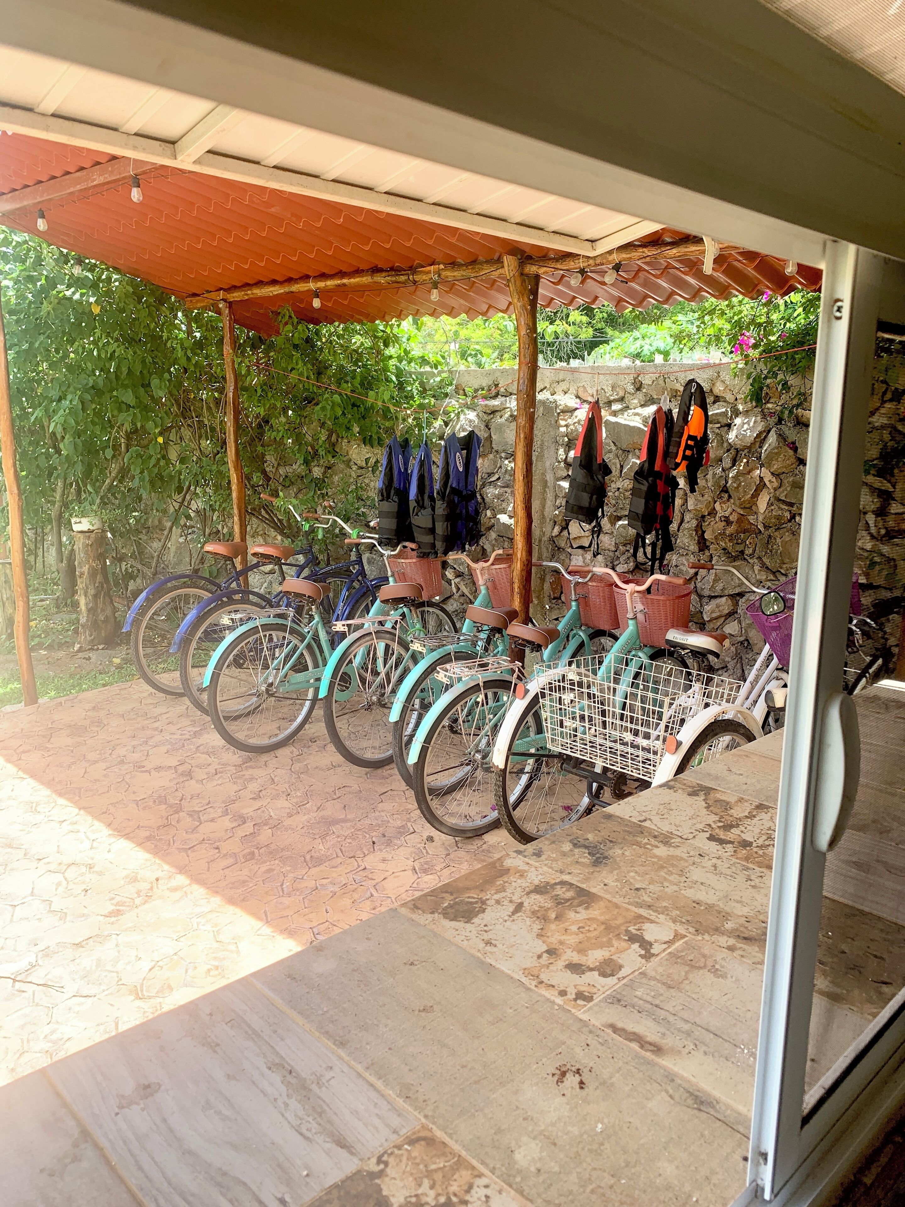 Un espacio al aire libre techado con bicicletas estacionadas bajo un refugio, un muro de piedra y un piso de madera.