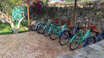 Varias bicicletas estacionadas bajo una zona techada, con un muro de piedra al fondo.