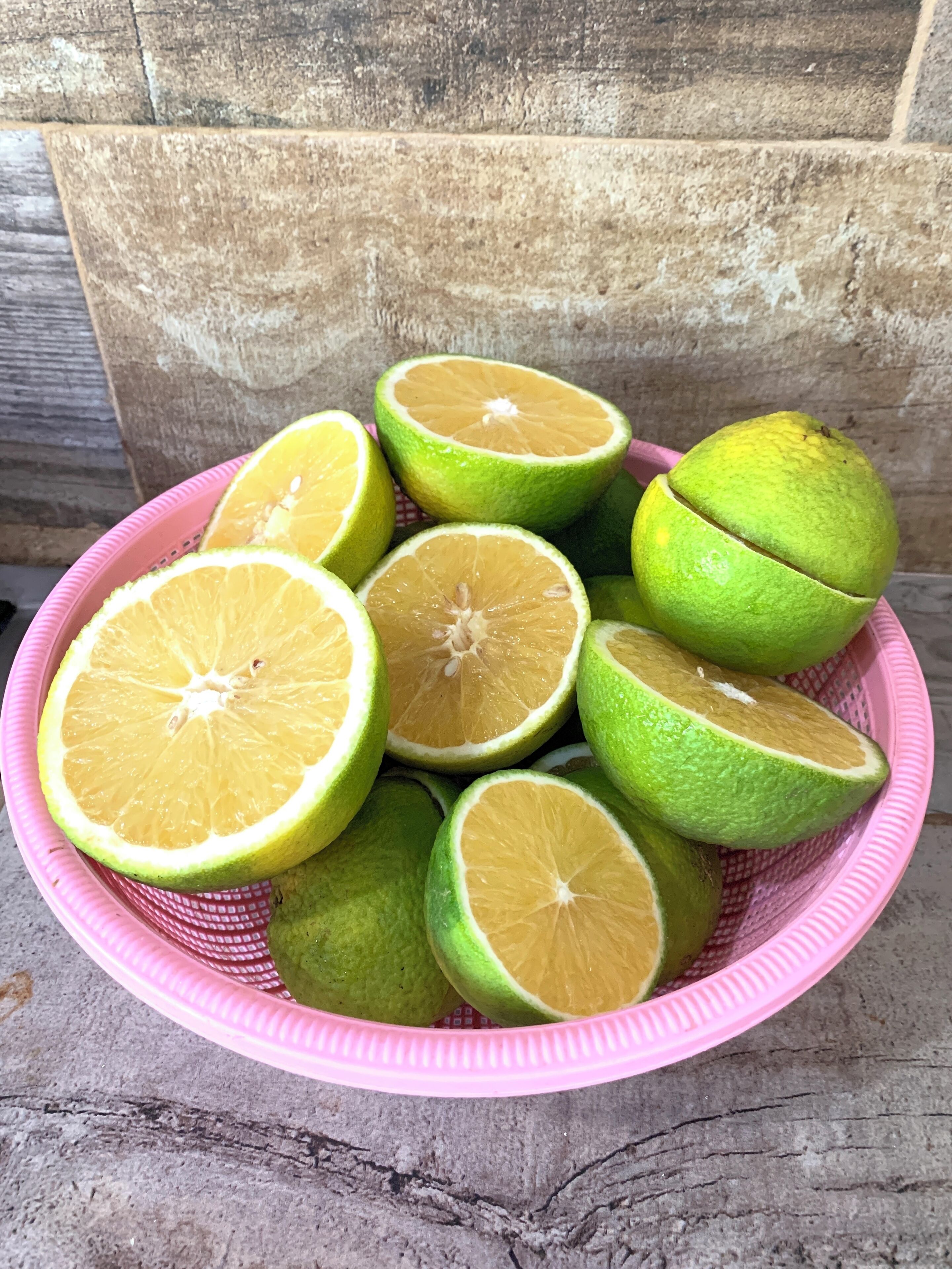 A pink basket filled with green limes, some cut in half, placed on a wooden surface.