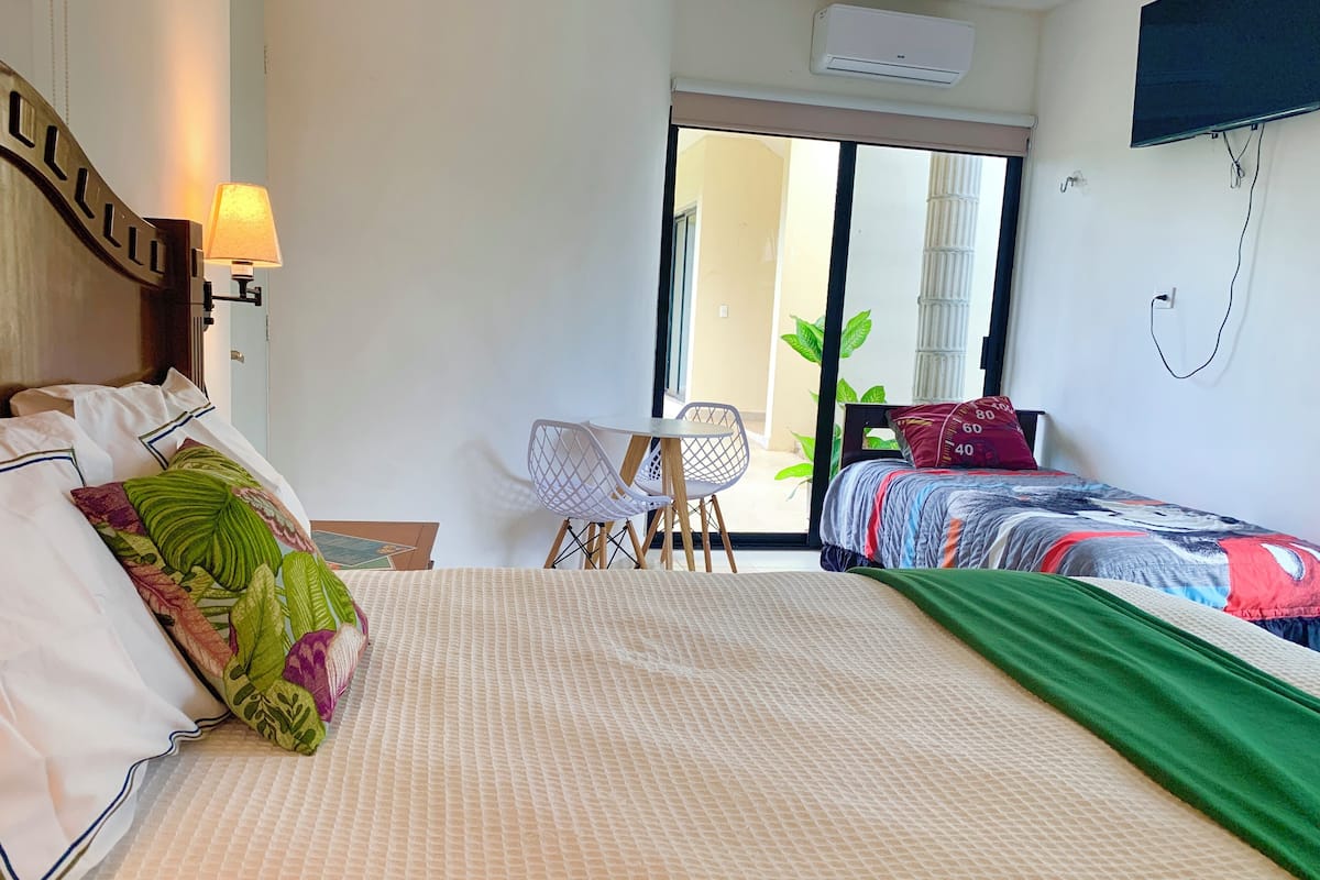 Una camera d'albergo con un letto grande, un tavolino con sedie, una TV e una porta scorrevole in vetro che dà sull'esterno.
