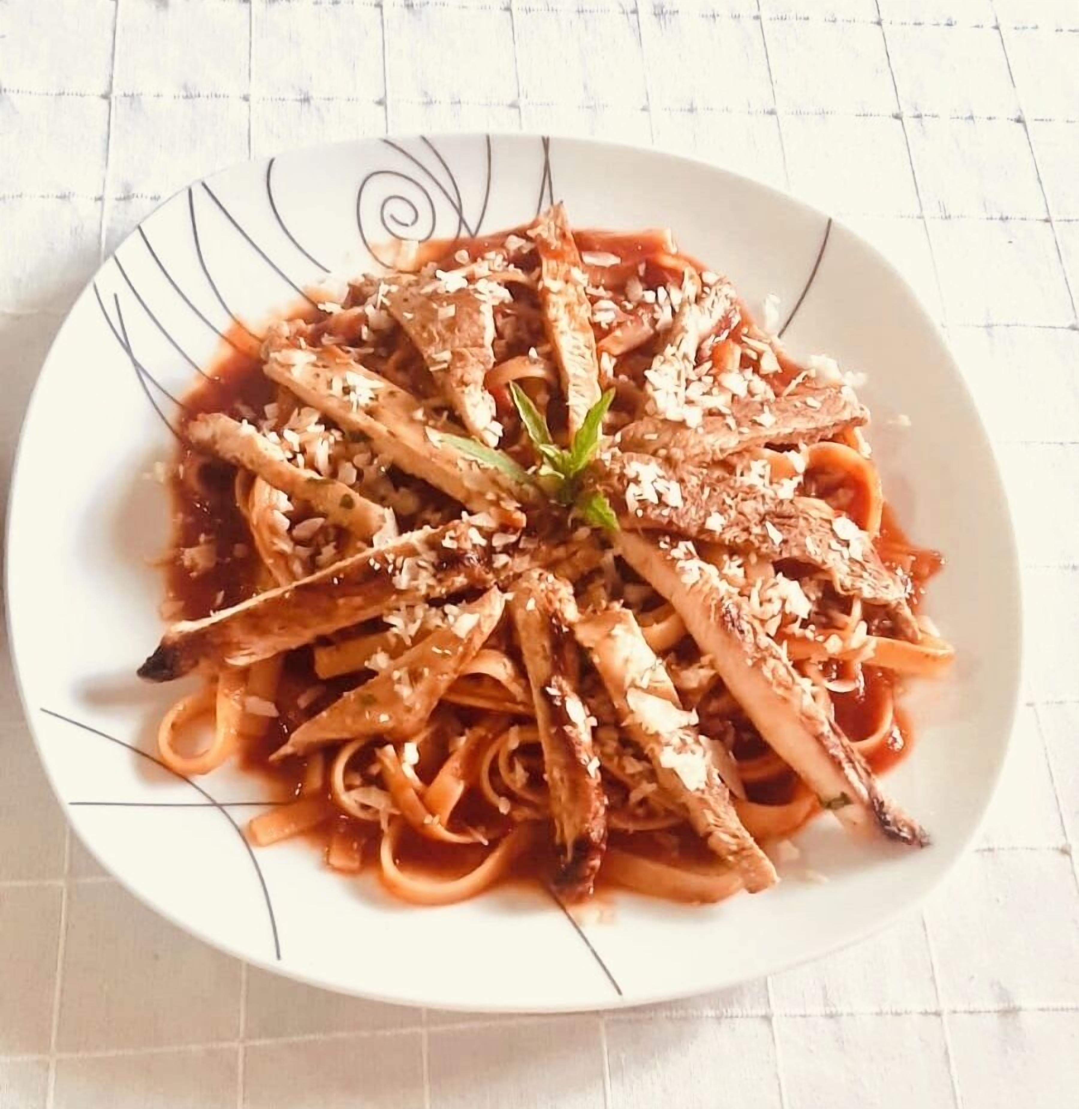 Pasta med kød og pynt på en hvid tallerken med dekorativ kant.