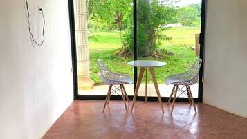 A room with a large sliding glass door leading to a garden, a small table with two chairs, and a bed with a green bedspread.