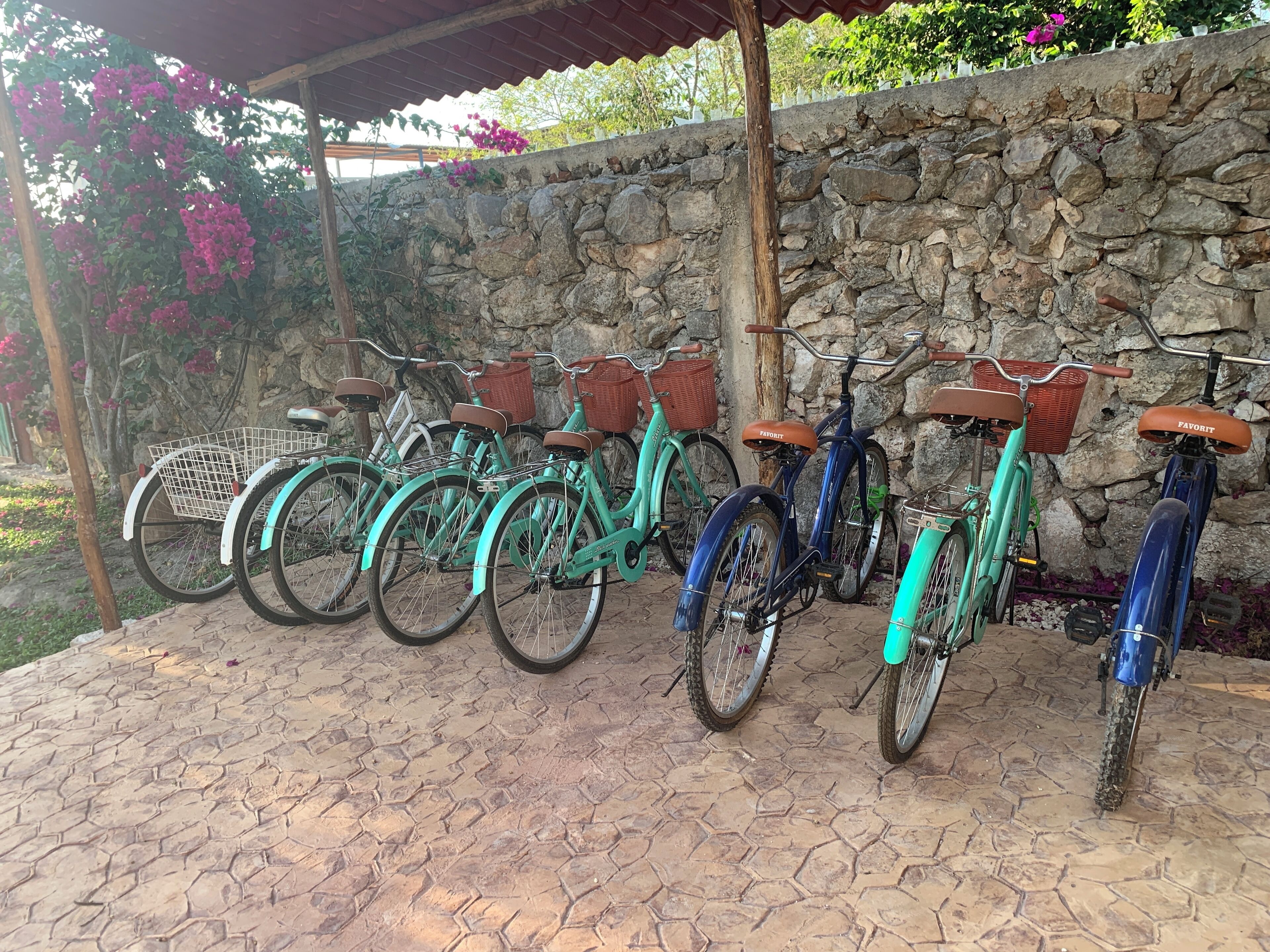 Varias bicicletas estacionadas junto a una pared de piedra y un suelo de baldosas.