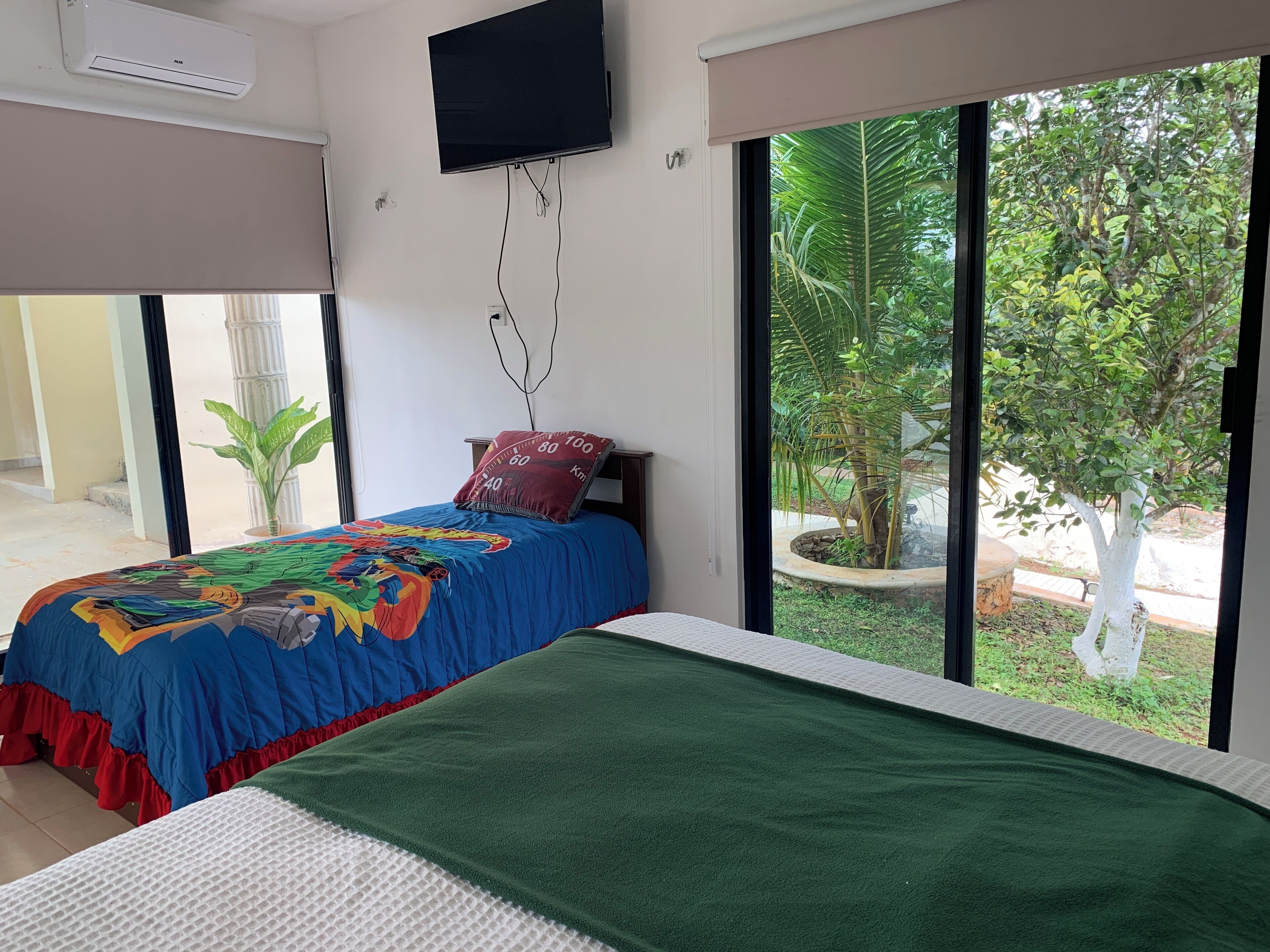 A bedroom with a bed, a TV, and a view of greenery outside.