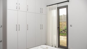 A bedroom with a large wardrobe, a bed with a rolled white towel, and a view of a garden through a sliding door. - Cozy Christina Apartment ground floor (Kissamos)