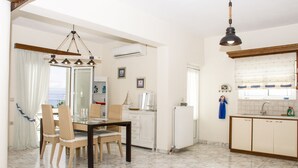 A dining area with a table and chairs, a kitchen with a sink and cabinets, and an air conditioning unit. - Christina Apartment 2nd Floor (Kissamos)