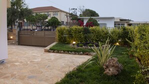 A courtyard with a stone patio, a gated entrance, and a well-maintained garden with various plants and a rock feature. - Christina Apartment 1st Floor (Kissamos)