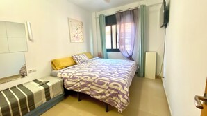 A bedroom with a bed, a ceiling fan, a window with curtains, a wall-mounted TV, and a radiator. - Estancias Mensuales Terrassa (Terrassa)