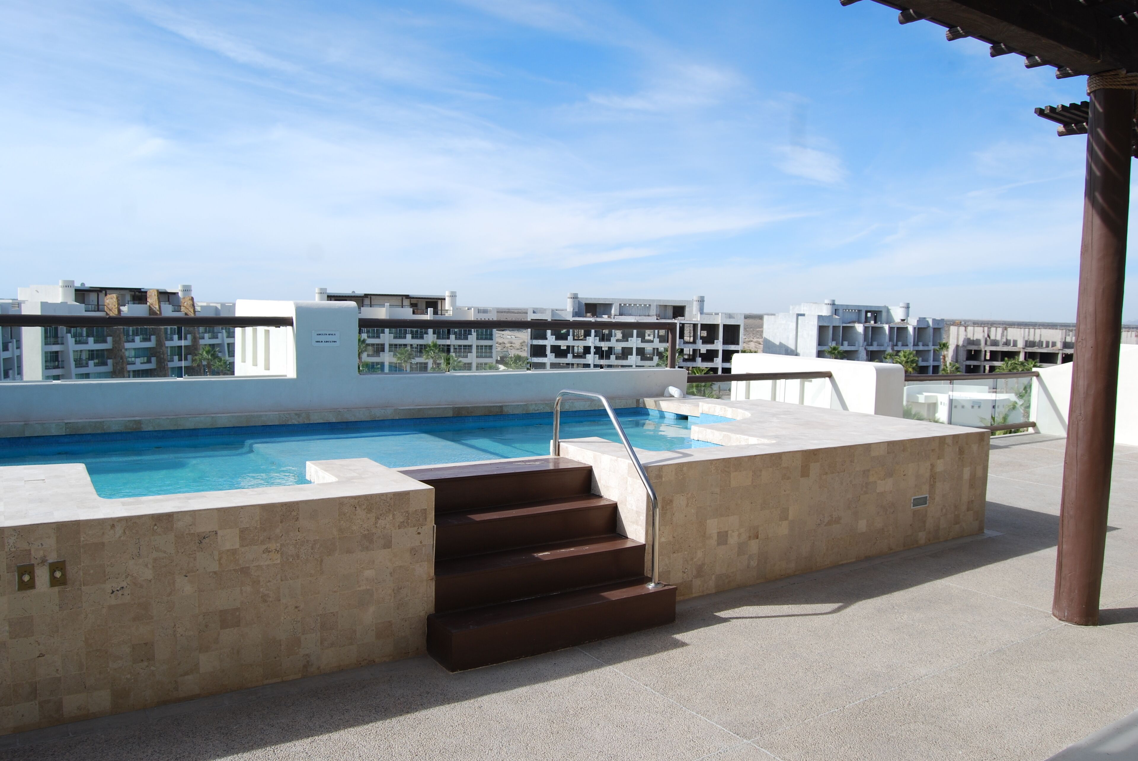 A rooftop pool with steps leading to the water, surrounded by a tiled deck and a view of modern buildings in the background.