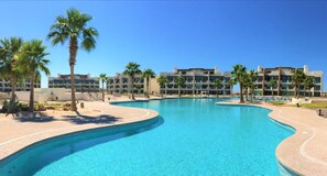 A large, curved swimming pool surrounded by palm trees and modern buildings.