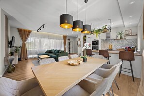 A modern living room with a wooden dining table, a sofa, and a kitchen area with a countertop and hanging plants. - Villa Animo - New holiday home for 8 people with a private pool near Labin. (Labin)