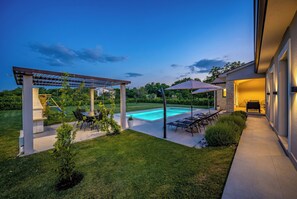 Un patio trasero con piscina, mobiliario de exterior y un pérgola.