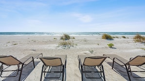 Une plage avec quatre chaises longues donnant sur l’océan, un ciel dégagé et des vagues douces.