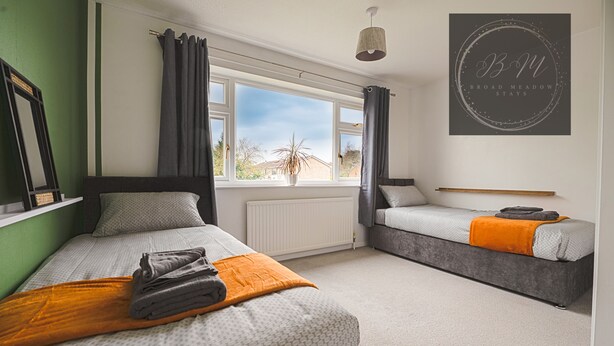 Een slaapkamer met twee bedden, een raam met gordijnen, een radiator en een bordje aan de muur.