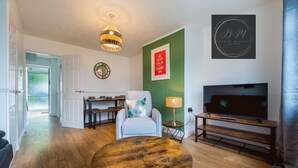 Een woonkamer met een ronde houten tafel, een televisie en een groene accentmuur.