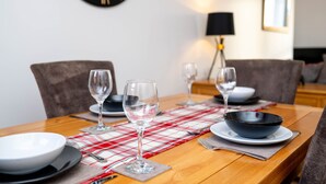 A dining table set with plates, bowls, and wine glasses, a clock on the wall, and a lamp in the background. - Heart of the City, Beautiful 3 bed 2 Bath, Sleep 6 (Lincoln)
