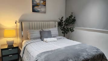 Ein Schlafzimmer mit Bett, Nachttischen, einer Lampe, einer Pflanze und einem Bild an der Wand.