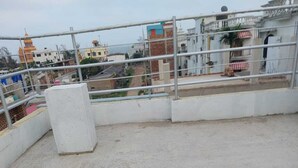 A rooftop terrace with a metal railing, concrete floor, and a view of surrounding buildings. - BLUESTONE HOTEL & RESTAURANT (Kanthi)