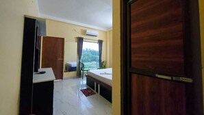 A room with a bed, a desk, a chair, and a window with curtains. - BLUESTONE HOTEL & RESTAURANT (Kanthi)